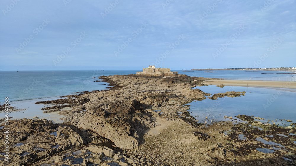 Photograph of coastal beach landscape with rock formations with the National Fort in Saint Malo