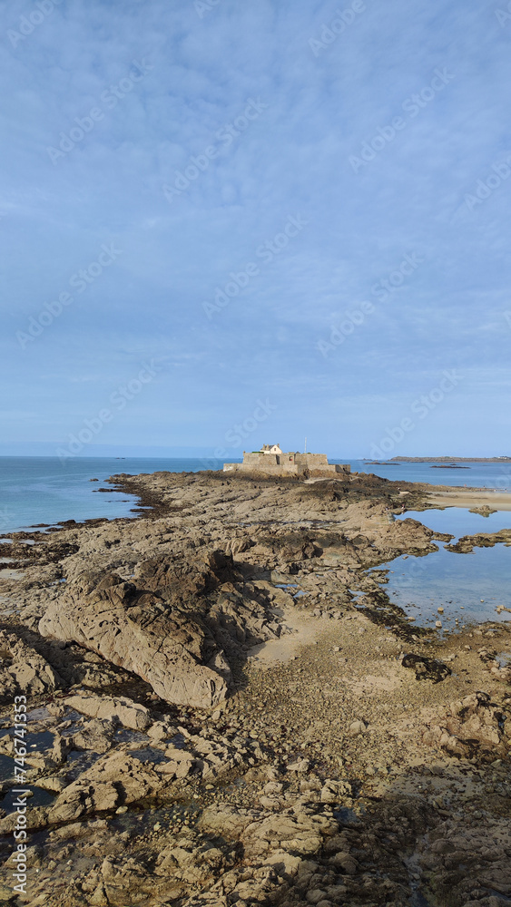 Photograph of coastal beach landscape with rock formations with the National Fort in Saint Malo