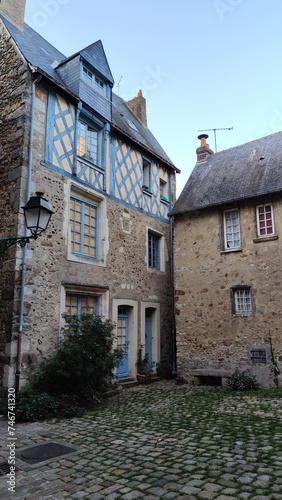 Vertical photo of the picturesque alleys of the old town of Le Mans in France, old style interior courtyard, stone houses with blue wooden doors and windows. There is a street lamp and cobblestones