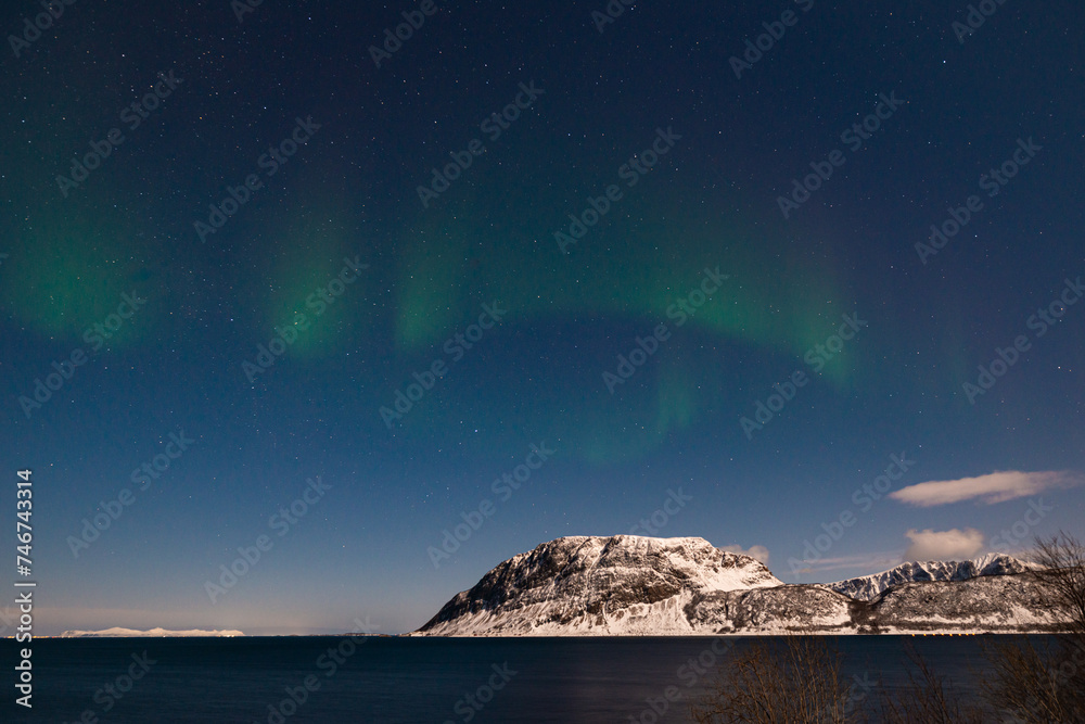 Green colored northern lights dance in the sky above snowy mountains on the Lofoten Islands in Norway