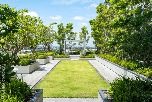 A neatly manicured rooftop garden pathway leading to a modern pergola with a panoramic city view.