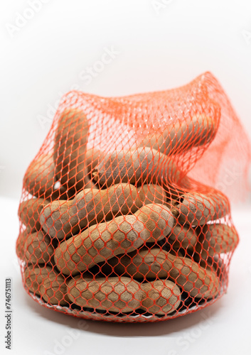 A red mesh bag full of sweet tamarind on a white background, representing fresh produce shopping.
