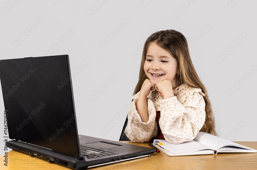 The little girl is smiling, sitting at a desk, using a laptop computer The little girl is smiling, sitting at a desk, using a laptop computer