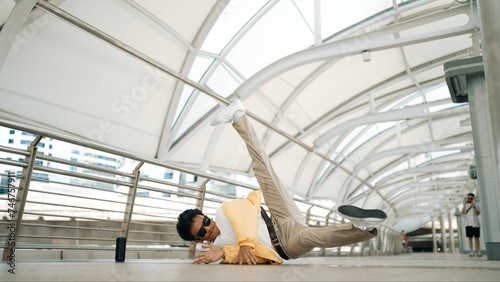 Handsome happy asian hipster dancing while using head spin at corridor. Break dancer or choreographer looking at camera while perform street dancing. Freestyle song. Outdoor sport 2024. Sprightly.