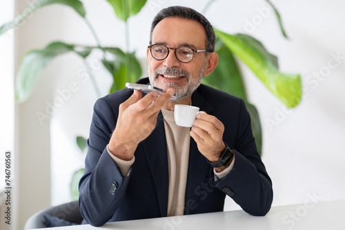 Cheerful mature businessman in glasses using voice command on his smartphone