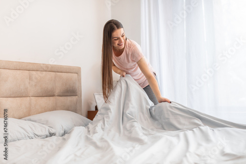 Cheerful woman making bed in bright room, displaying everyday domestic life photo