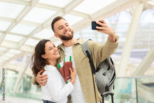 Travel Selfie. Portrait Of Cheerful Couple Taking Photos On Smartphone In Airport