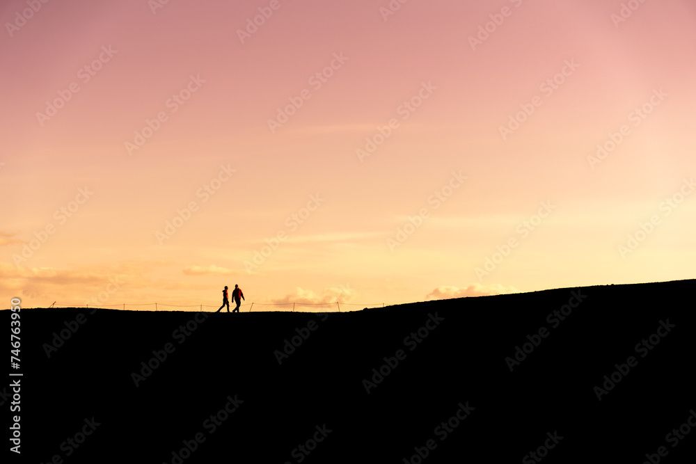 Unknown couple hiking in silhouette at sunset