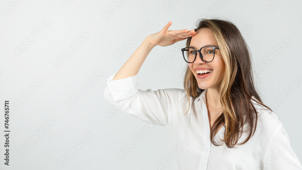 An exuberant young woman with glasses, wearing a white blouse, is looking into the distance with her hand