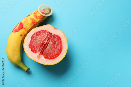 Half of grapefruit, banana with condom and red lipstick marks on light blue background, flat lay with space for text. Safe sex concept