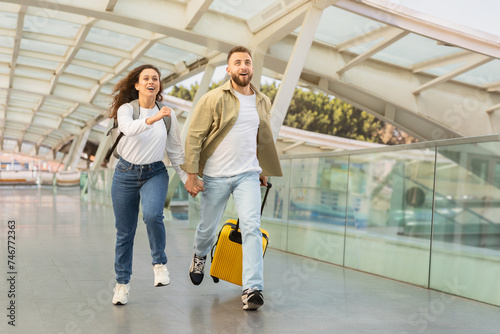 Young couple in rush running with yellow suitcase at the airport