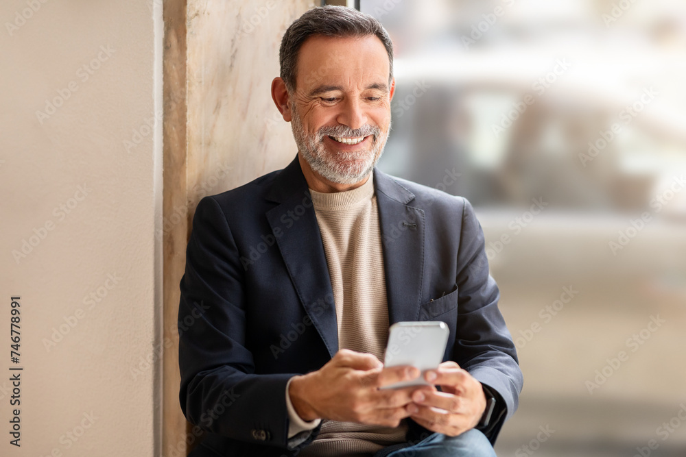 Smiling senior businessman in a stylish blazer using his smartphone Smiling senior businessman in a stylish blazer using his smartphone