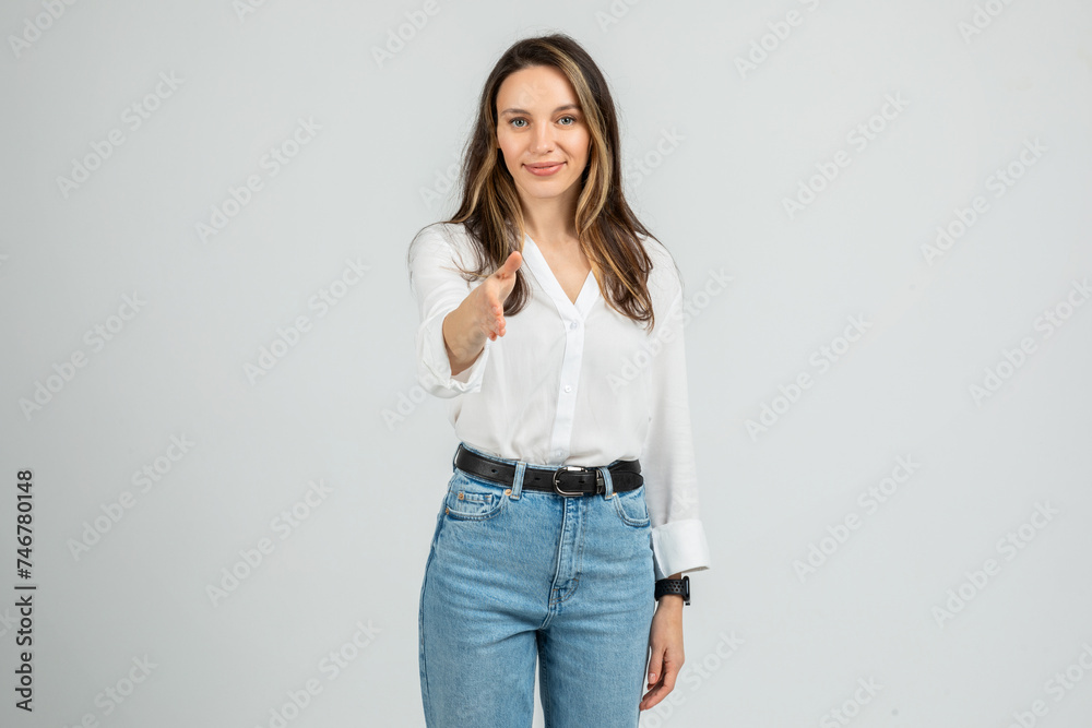 A young woman with long hair wearing a white blouse and blue jeans stands smiling A young woman with long hair wearing a white blouse and blue jeans stands smiling