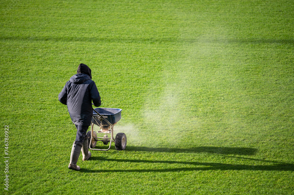 Groundsman spreads fertilizer for grass on a football pitch