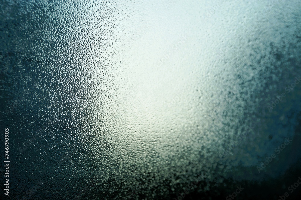 Abstraktes Motiv mit Eisbedeckter Glasscheibe vor blauem Himmel mit weißer Sonne bei Kälte, Frost und Sonne am Morgen im Winter