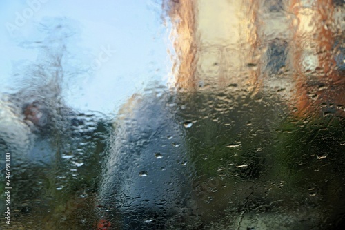 Abstraktes Motiv mit Regentropfenmuster vor Rückenansicht von frau mit grauem Anorak auf Gehweg zwischen Vorgärten und Häusern vor Himmel bei Regen, Nebel und Kälte am Morgen im Winter