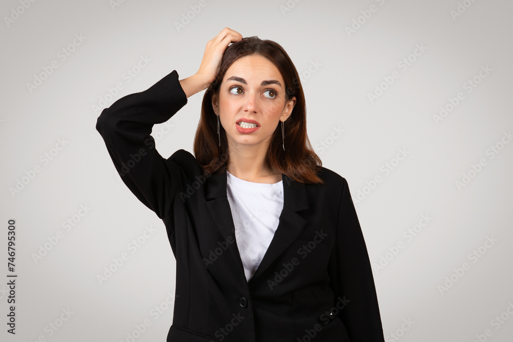 Puzzled young businesswoman in a black suit with a white shirt scratching her head with a perplexed expression Puzzled young businesswoman in a black suit with a white shirt scratching her head with a perplexed expression