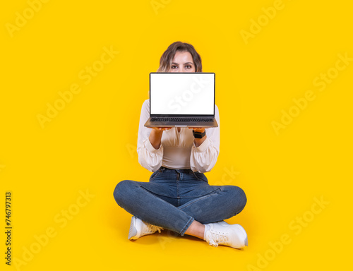 Demonstrating laptop mock up, full body portrait of young caucasian woman sit floor demonstrating laptop mock up. Young girl showing empty screen pc computer holding it in front of her face.