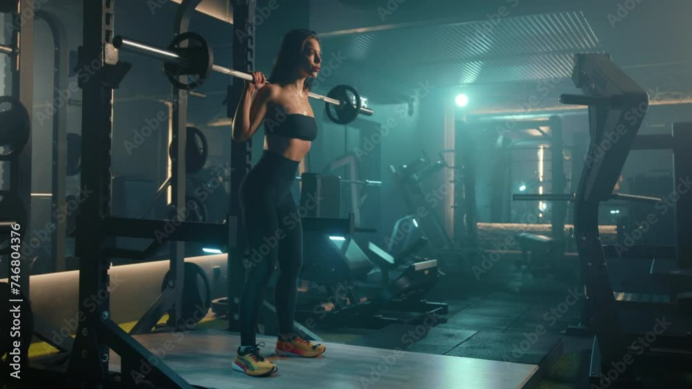 A young and dedicated sportswoman squatting with a barbell, working on her lower body strength in a modern, well-lit gym full of various equipment. Camera 8K RAW. A young and dedicated sportswoman squatting with a barbell, working on her lower body strength in a modern, well-lit gym full of various equipment. Camera 8K RAW.