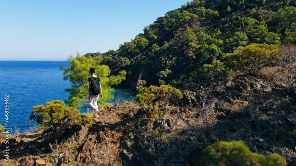 Young women with backpack are climbing cliff on seacoast, climb the high rock Young women with backpack are climbing cliff on seacoast, climb the high rock
