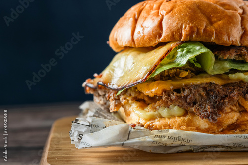 Deliciosa hamburguesa con doble carne aplastada, doble queso sobre tabla de cocina en una mesa de madera rústica en un fondo azul tomada de cerca