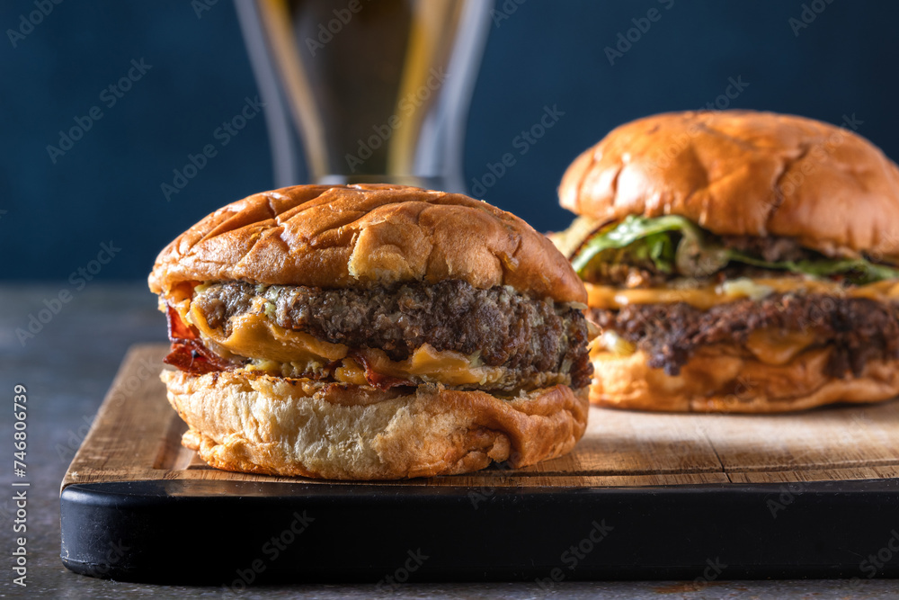 Dos deliciosas hamburguesas de carne aplastada sobre tabla de cocina en un mesón de granito viejo con una cerveza tomada de cerca