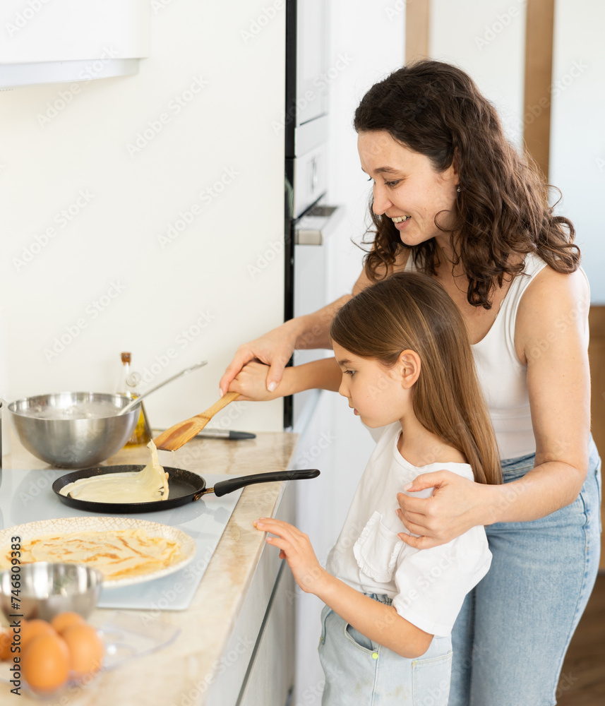 Girl is naughty while cooking pancakes with her mother. Woman and girl fry pastry dessert in frying pan and have fun, communicate.