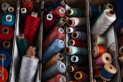 Blurred image of spools of multi-colored sewing threads in a box.