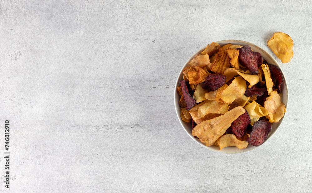 A bowl of vegetable organic chips made from beets, carrots and celery root on a gray background. Top view. Copy space A bowl of vegetable organic chips made from beets, carrots and celery root on a gray background. Top view. Copy space