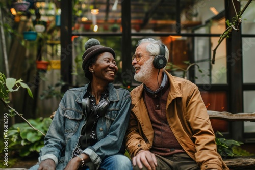 A content senior couple, each with headphones, enjoy a quiet moment together amidst the lush greenery of a garden conservatory.