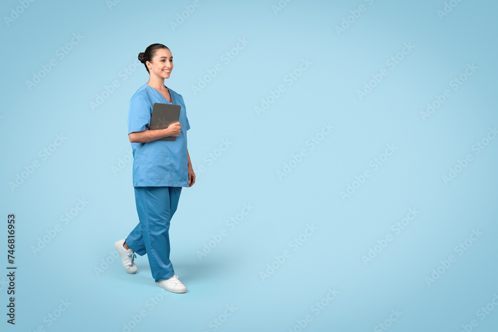 Smiling young female nurse walking with tablet on blue, free space Smiling young female nurse walking with tablet on blue, free space