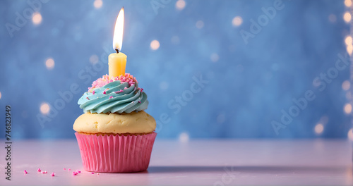 Un petit cup cake en forme de gâteau d'anniversaire avec de la crème et une bougie allumée sur un fond bleu et rose dans une ambiance festive