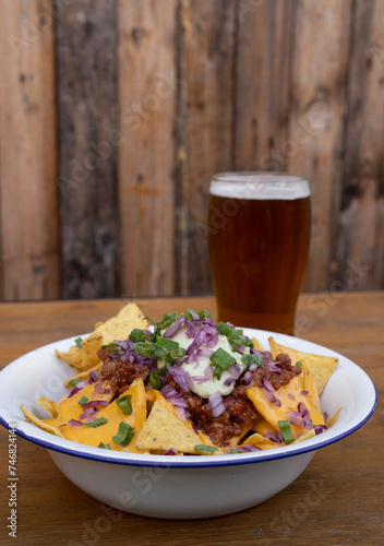 Nachos with chili. Closeup view of nachos with cheddar cheese, avocado cream, red onion pickles and meat sauce in a white bowl with a wooden background.