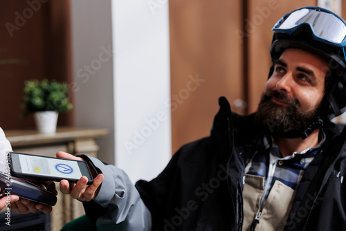 Slika na platnu In ski resort lounge area, caucasian man pays with cell phone while staff assists with pos machine