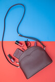 Woman's leather handbag in crimson color and accessories on red and blue background. Top view.