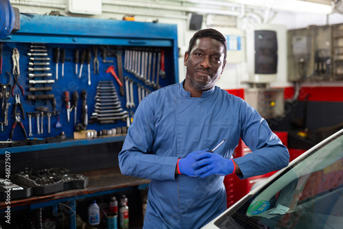 Professional man car mechanician standing near repairable car in auto repair shop photo