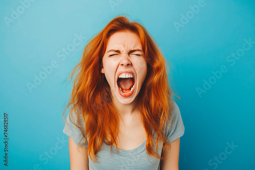The young emotional angry woman screaming on blue studio background.