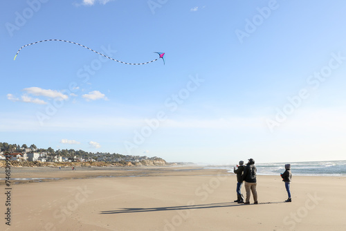 Dad and teenagers flying kites together on the beach at sunset.  Stunt kit with beautiful sky and ocean in the background.
