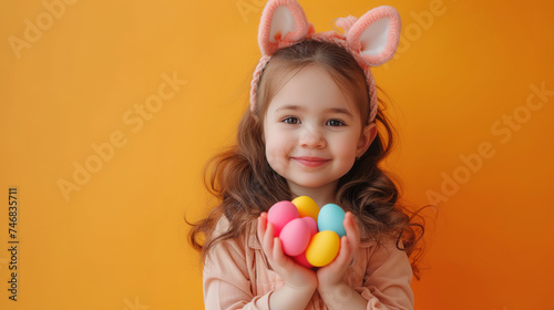 Easter joy: girl with bunny ears holding colored eggs on orange background