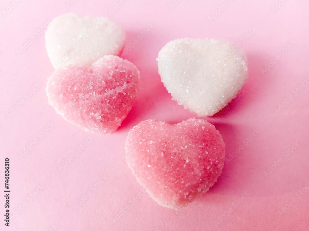 a group of pink and white heart-shaped chewy candies on a pink background. chewy candy sprinkled with granulated sugar. sweet and chewy
