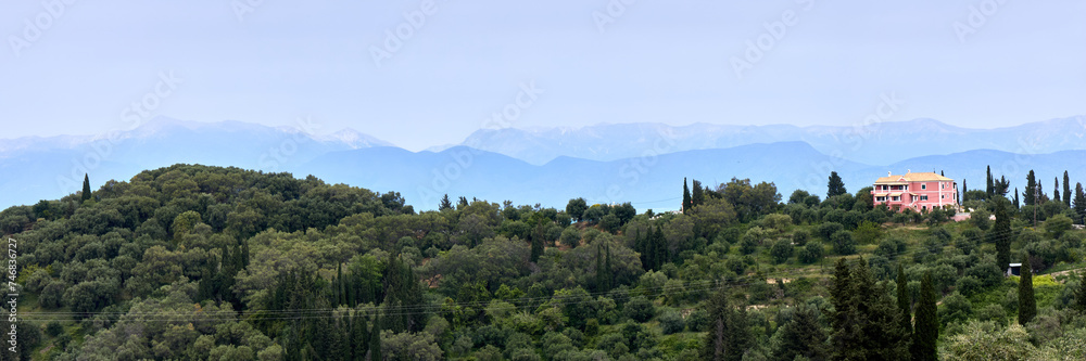 Green hills on the seashore and the silhouettes of the mountains on the horizon. View from the Greek island of Corfu to the mountains on the coast of Albania