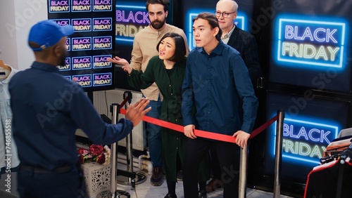 Crazy clients pushing man on floor during black friday sales, crowd of obsessed mad customers acting aggressive in line. Young man falling down at clothing store entrance, red tape.