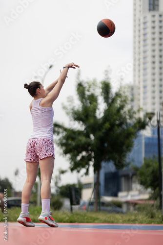 Girl playing basketball. Player throwing ball. Outdoor sports field in urban surroundings.