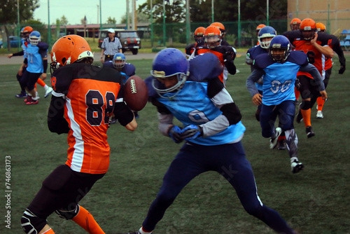 An American football player in a black and blue uniform hits a player in a black and orange uniform with his shoulder on a green field