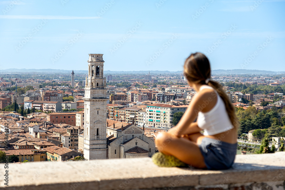 Defocused young traveler girl sit on the top of Colle San Pietro (Saint Peter's Hill) looking at the city of Verona in a beautiful sunny day; Veneto, Italy