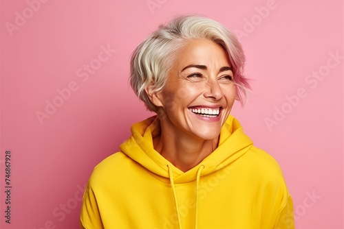 Portrait of a happy senior woman in yellow hoodie over pink background