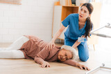senior patient falling on the ground floor at home, Asian caregiver helping elderly older female from accident after doing physical therapy then rescued by attractive therapist nurse, health insurance