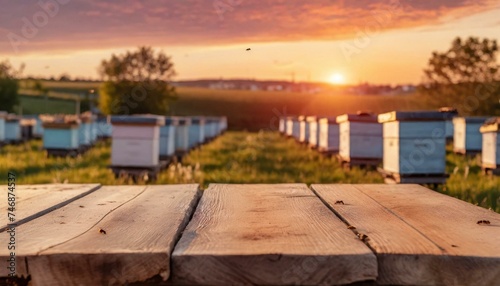 Empty wooden table top for product display. In the background  a blurred background of a small apiary at sunset