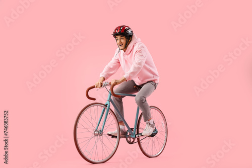 Fototapeta Naklejka Na Ścianę i Meble -  Young man in helmet riding bicycle on pink background