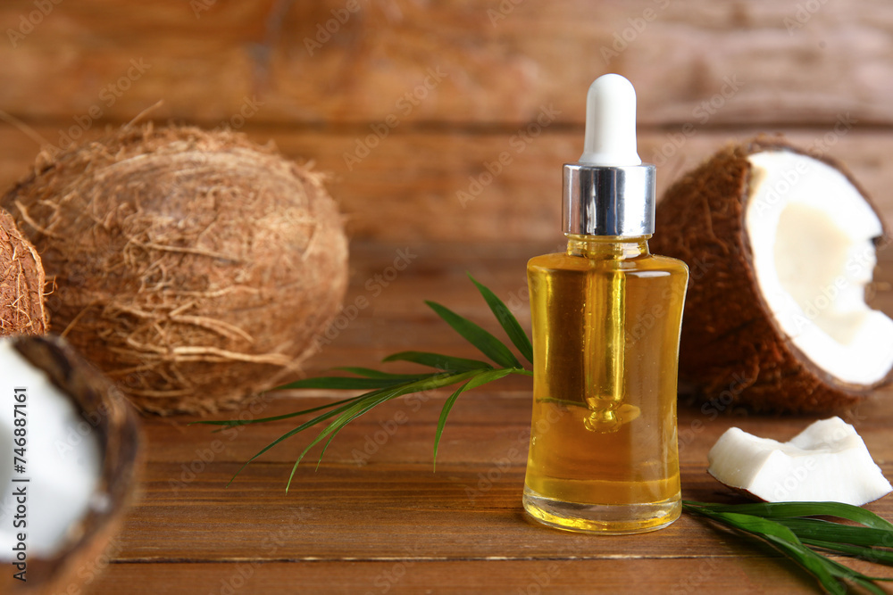 Bottle of coconut cosmetic oil with plant leaves on brown wooden background Bottle of coconut cosmetic oil with plant leaves on brown wooden background